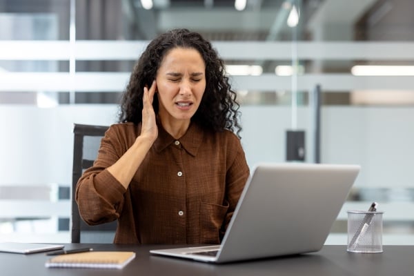 Frau verspürt Tinitus am Arbeitsplatz