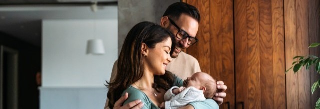 Frischgebackene Mutter mit Kind und Vater im Hintergrund