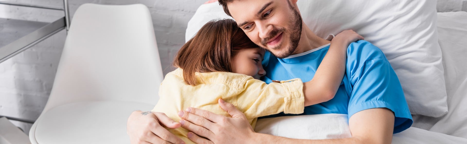 Vater im Krankenbett umarmt Kind