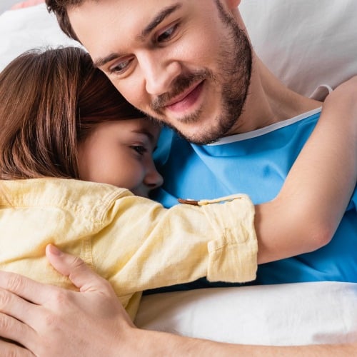 Vater im Krankenbett umarmt Kind