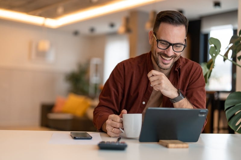 Mann mit Kaffee in der Hand lächelt in den Laptop