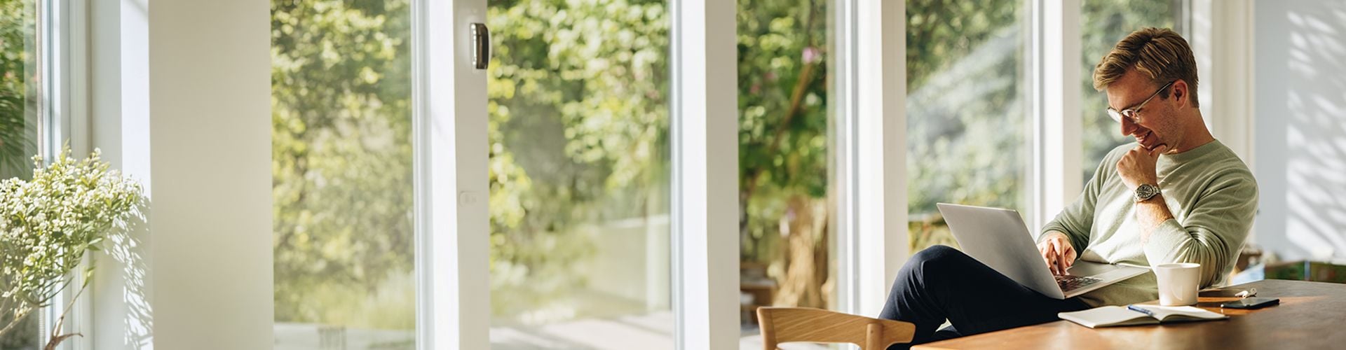 Mann sitzt beim Esstisch und schaut auf Laptop