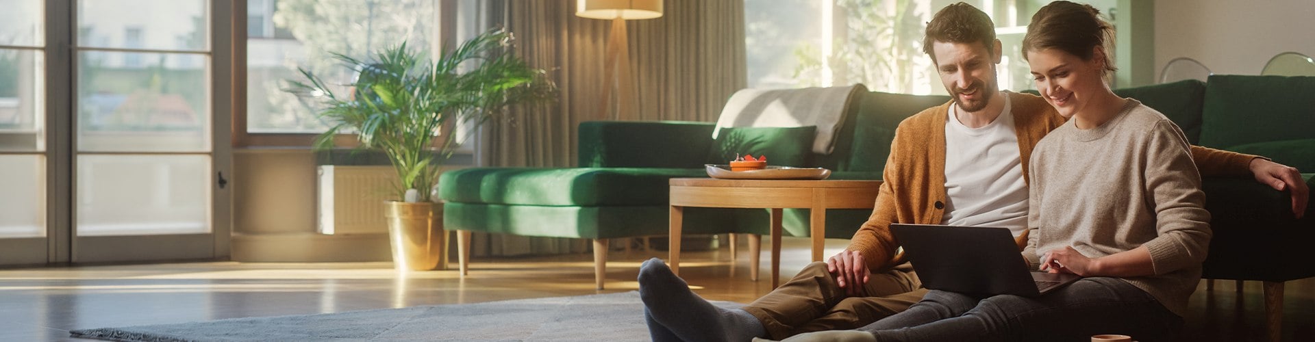 Paar sitzt auf Boden vom Wohnzimmer und schaut in den Laptop