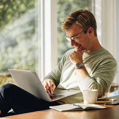 Mann sitzt beim Esstisch und schaut auf Laptop