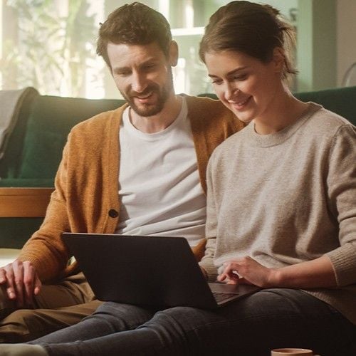 Paar sitzt auf Boden vom Wohnzimmer und schaut in den Laptop