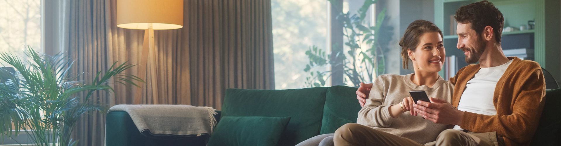 Paar sitzt auf der Couch und schaut sich an mit Handy in der Hand