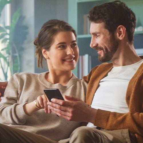 Paar sitzt auf der Couch und schaut sich an mit Handy in der Hand