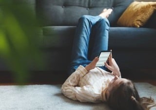 Kind liegt im Wohnzimmer und schaut aufs Handy
