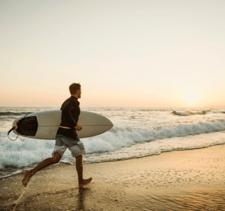 Surfer laufend am Strand Sonnenuntergang Reiseversicherung